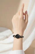 Close-up of a wrist wearing a black round dial watch with a crystal-studded linked strap on a light background