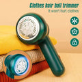 Electric clothes hair ball trimmer in dark green on folded knit sweaters, close-up of lint remover blades