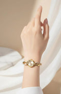 Elegant gold bracelet watch with crystal accents on wrist against soft beige background