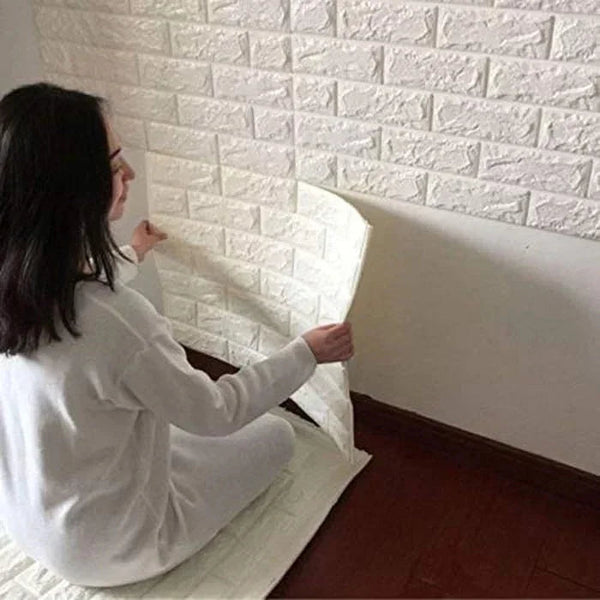 Woman installing peel and stick 3D white brick wall panels in a room with dark wood flooring